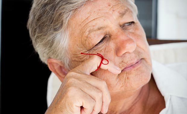 Eine ältere Frau mit einer roten Schleife um den Zeigefinger.